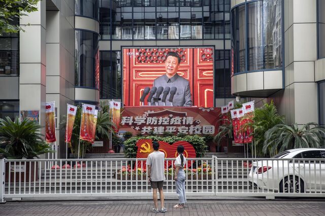 Pedestrians watch a screen showing a live news broadcast of Chinese President Xi Jinping speaking at a ceremony marking the centenary of the Chinese Community Party, taking place at Beijing's Tiananmen Square, in Shanghai, China, on Thursday, July 1, 2021.