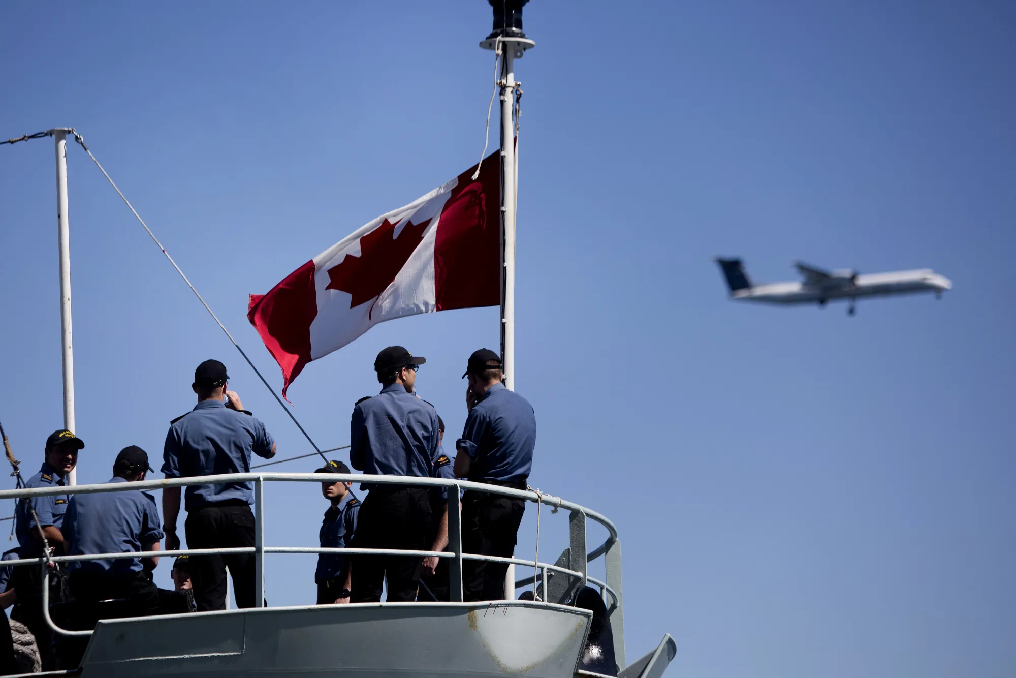 An airplane flies past a Canadian flag on a navy ship in Toronto.