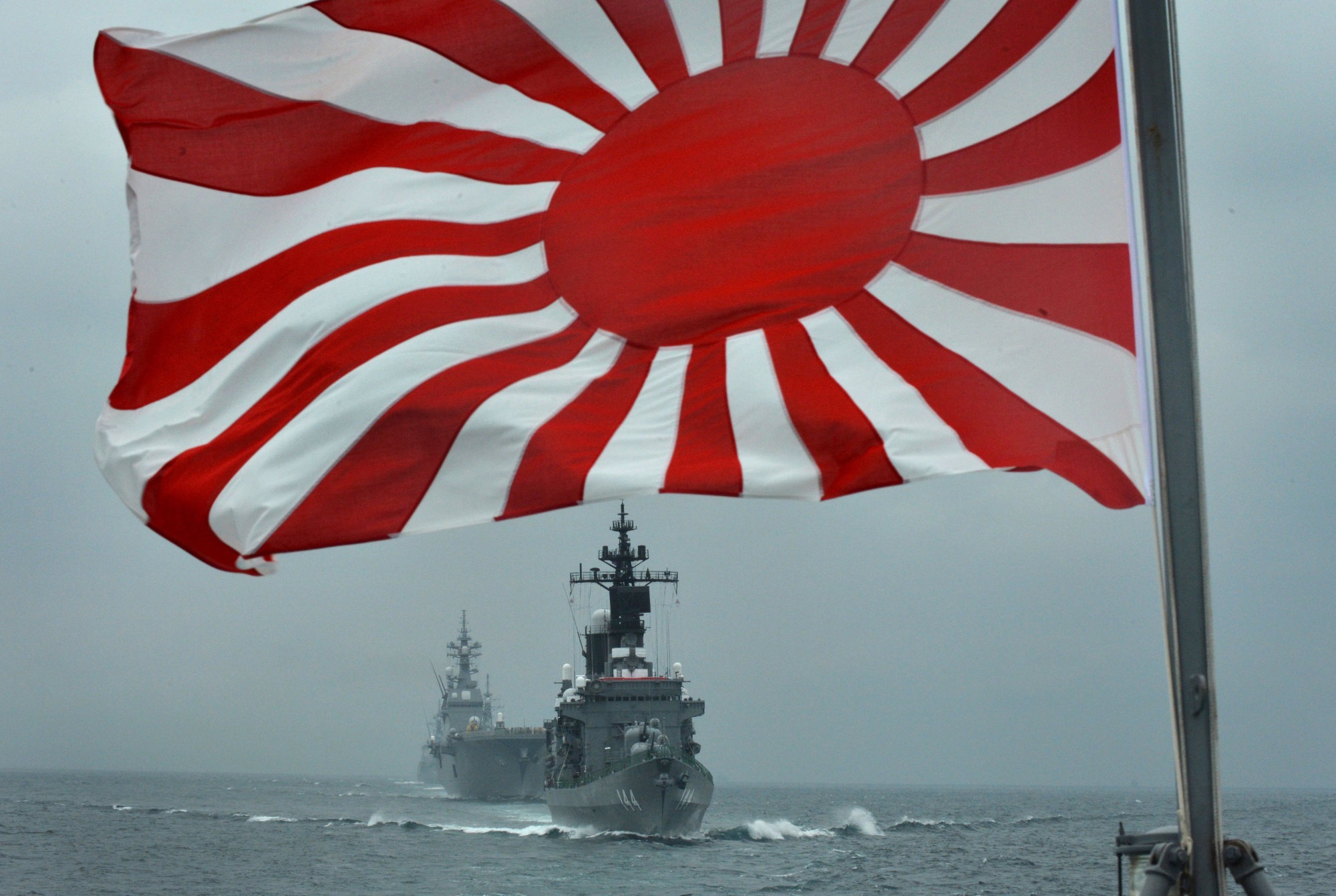 In this picture taken on October 14, 2012 a flag of the Japanese Maritime Self-Defense Force (MSDF) flutters in the wind as MSDF escort ships Kurama (R) and Hyuga (L) make its fleet review off Sagami Bay, in Japan's Kanagawa prefecture. - Japan decided on October 5 to cancel plans to participate in an international fleet review in South Korea, after Seoul demanded the removal of a controversial naval flag from Tokyo's warship. (Photo by Kazuhiro NOGI / AFP) (Photo credit should read KAZUHIRO NOGI/AFP via Getty Images)