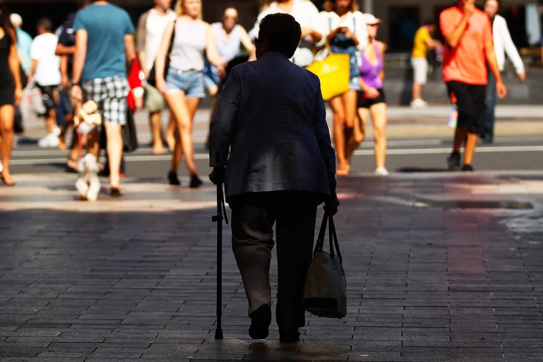 A woman holding a walking cane walks along a street in Sydney.