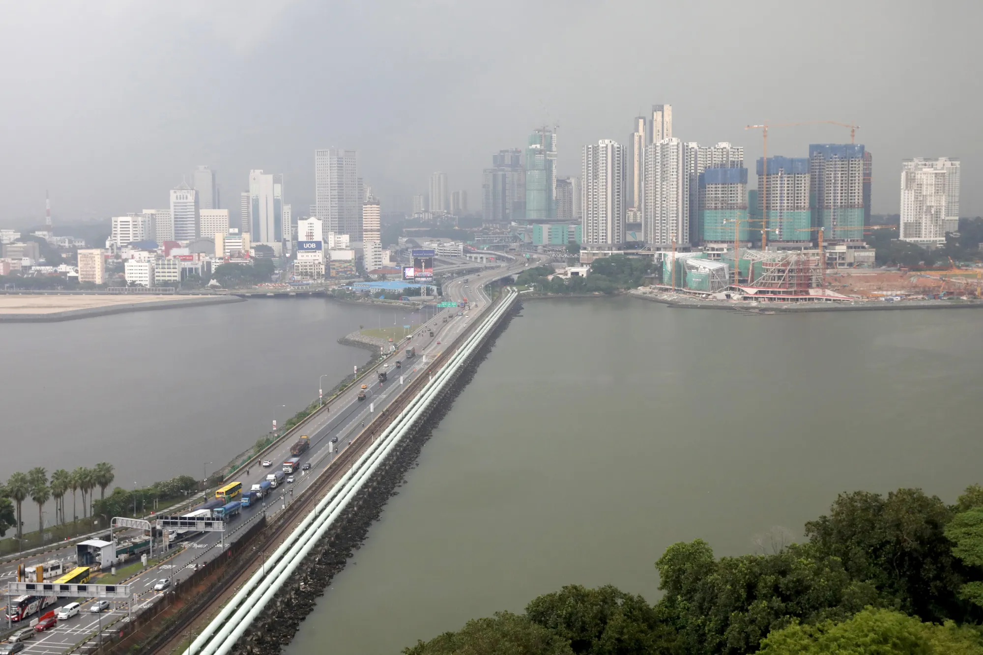 Vehicles travel along the Causeway across the Straits of Johor as commercial and residential buildings stand in the Malaysian city of Johor Bahru, background, as seen from Singapore.