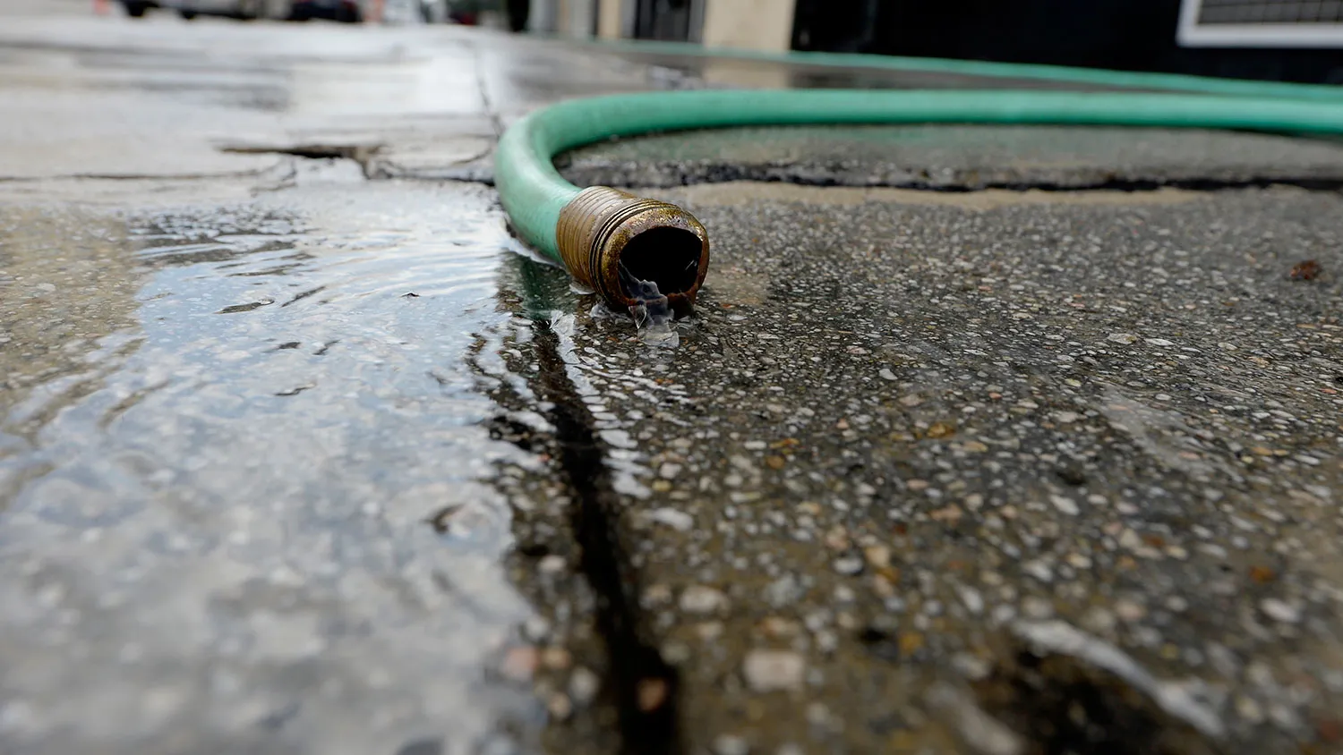 Water pours out of a hose after a worker washes the sidewalk in front of a business in downtown Los Angeles, California, U.S. on Friday, July 18, 2014.
