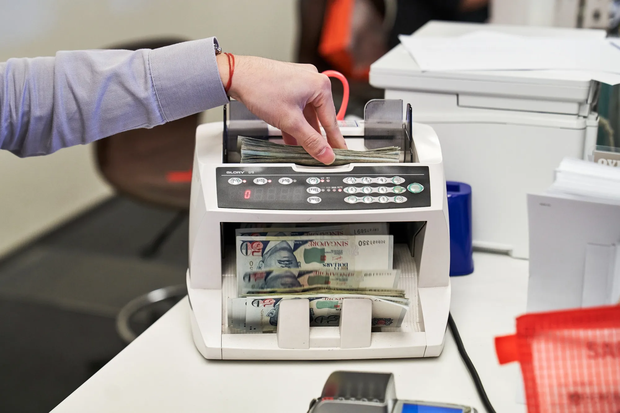 An employee puts Singaporean fifty-dollar banknotes into a money counting machine at the Oversea-Chinese Banking Corp. (OCBC) Centre Branch in Singapore, on Monday, Feb. 23, 2021. OCBC, which is scheduled to announce earnings on Feb. 25, last month appointed Helen Wong as chief executive officer to succeed Samuel Tsien. Photographer: Lauryn Ishak/Bloomberg