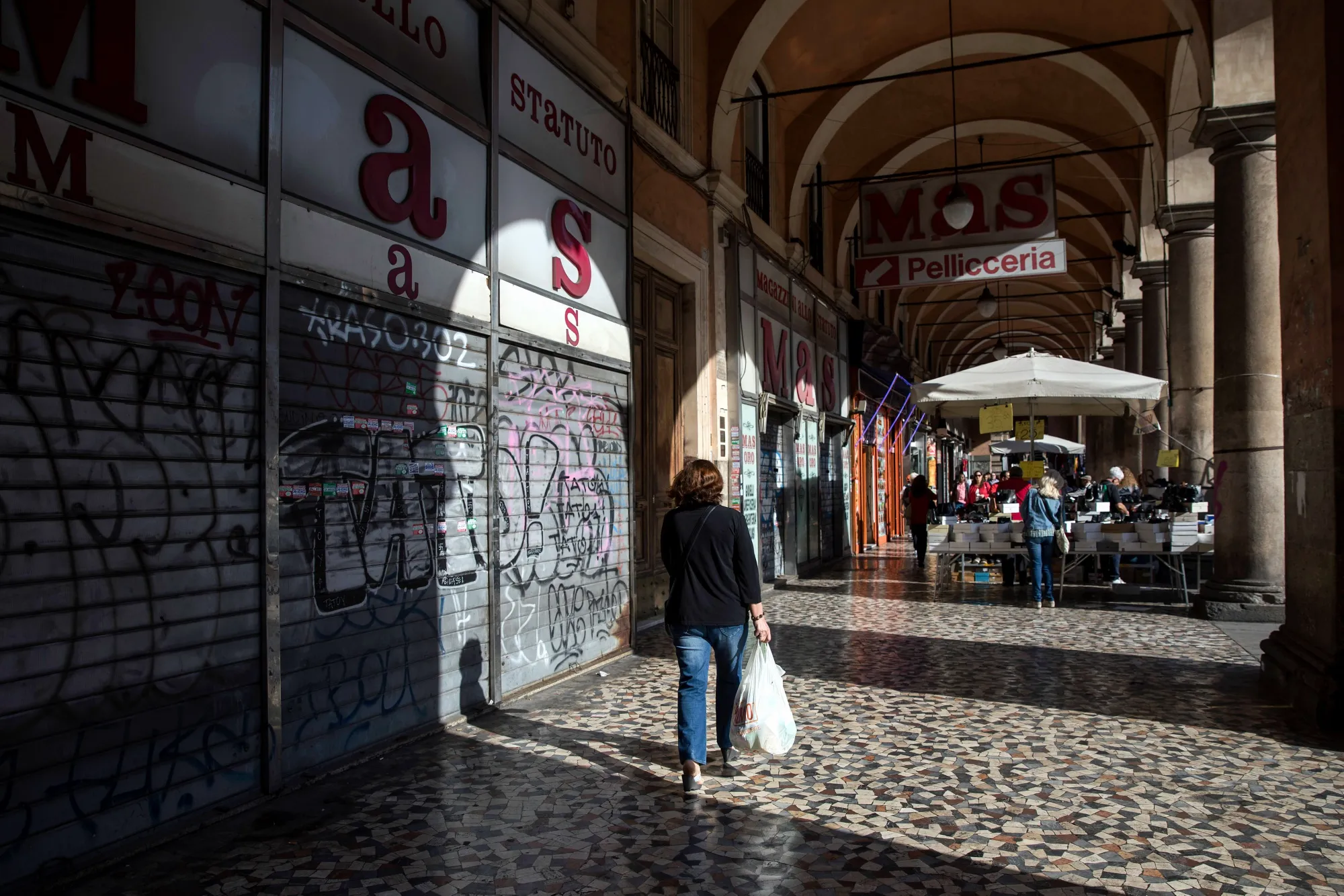 Pedestrians carry shopping bags near market stalls in Rome.