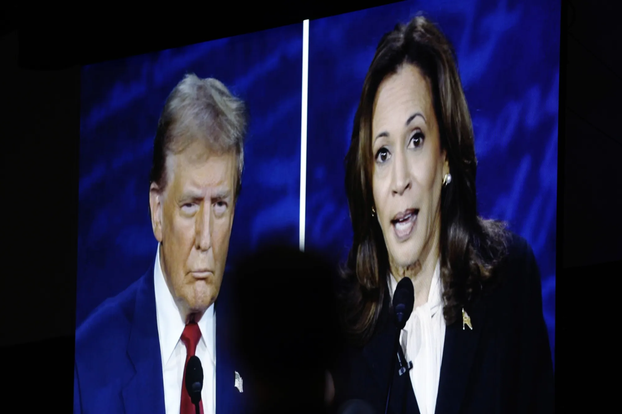 Donald Trump, on a screen,&nbsp;left, and Kamala Harris.