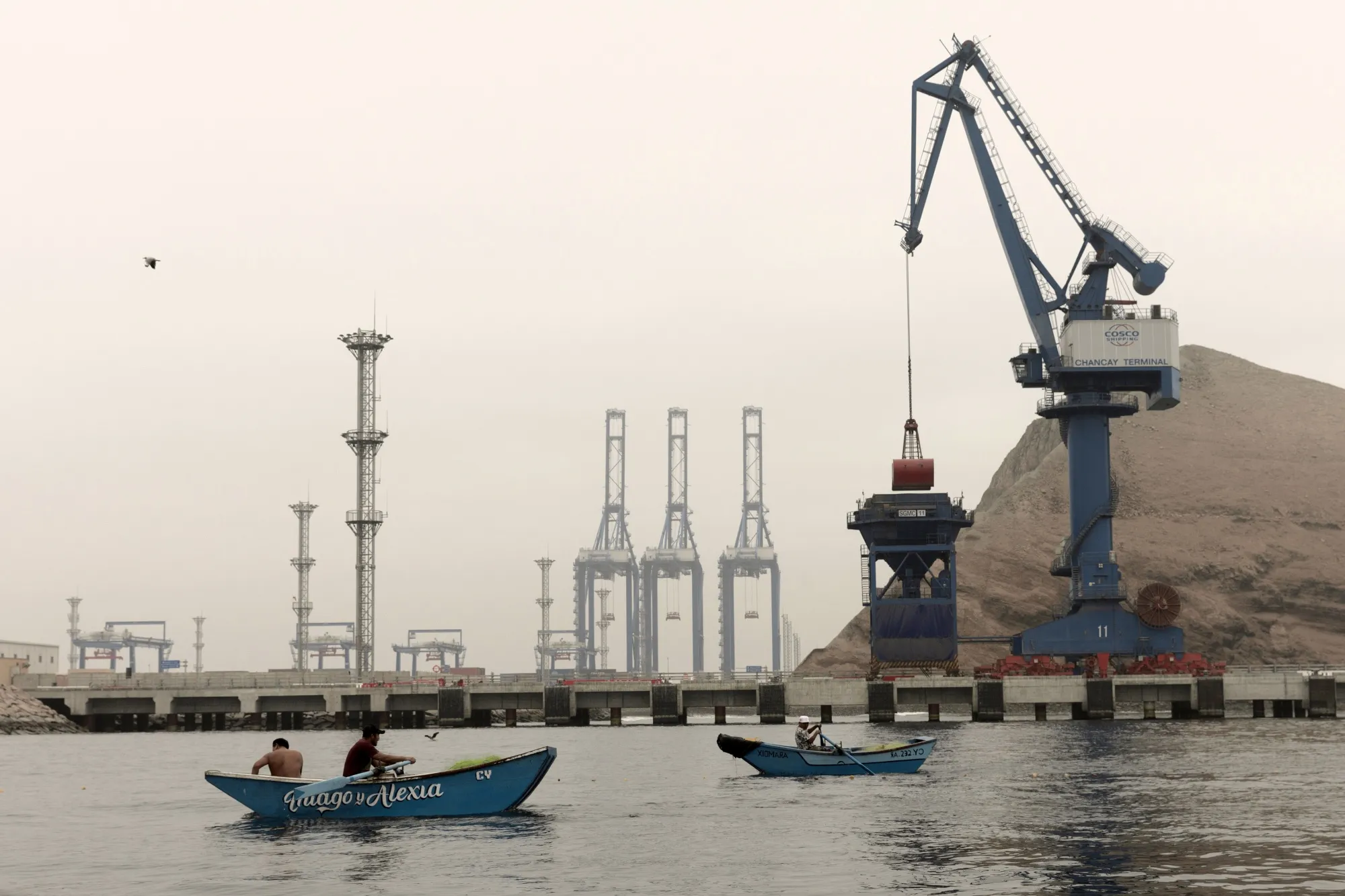 Fishermen row boats past the Chancay Port in Chancay, Peru.