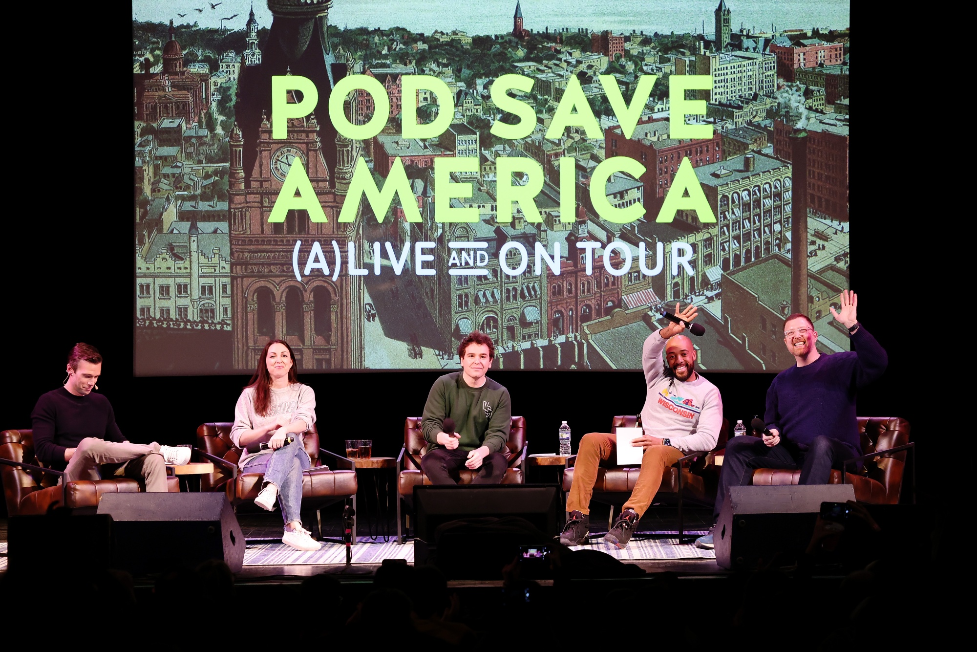 Hosts Jon Favreau, left,&nbsp;and Jon Lovett, third from left, speak onstage during the live taping of &quot;Pod Save America,&quot;&nbsp;earlier this year in Madison, Wisconsin. (Photo by Jeff Schear/Getty Images for WisDems)