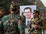 Syrian soldiers walk past a portrait of President Bashar al-Assad during a government celebration marking the first anniversary of the retaking of the northern Syrian city of Aleppo on Dec. 21, 2017.
