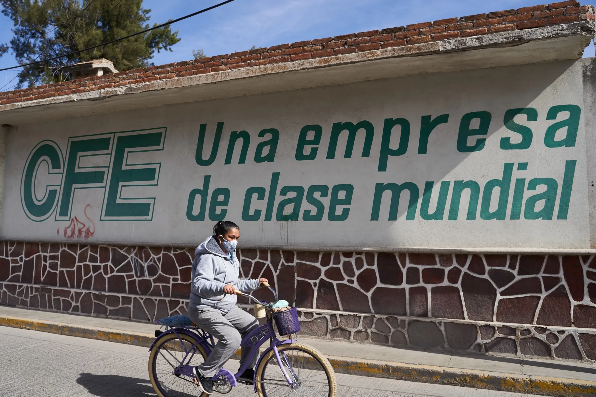 A person wearing a protective mask rides a bicycle past a Comision Federal de Electricidad (CFE) facility in Villa de Reyes, San Luis Potosi state, Mexico, on Tuesday, Jan. 19, 2021. 