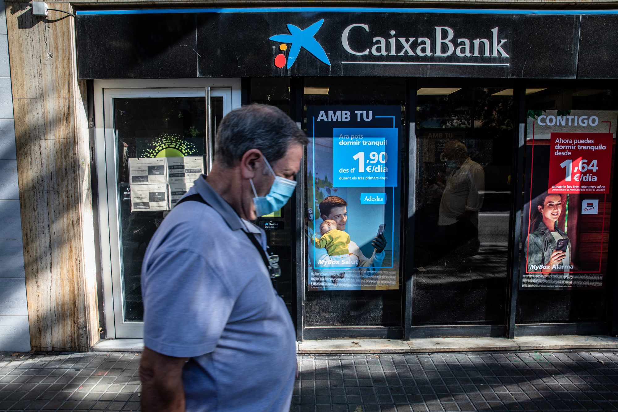 A pedestrian walks by a CaixaBank SA bank branch in Barcelona.