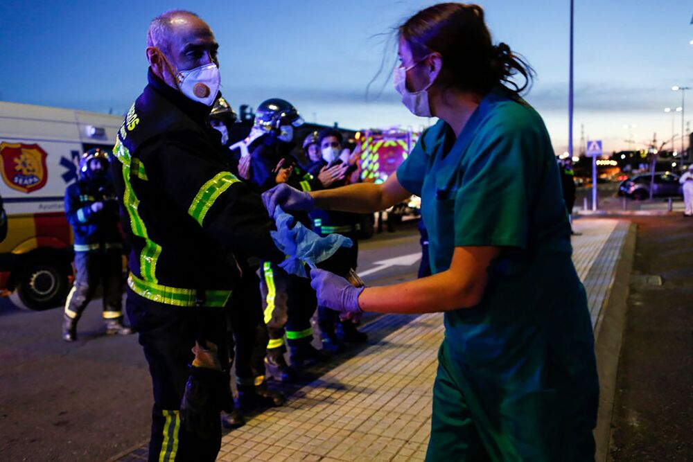 A sanitation worker ties a protective coat to the arm of a fireman as a symbol of gratitude for their support during Covid-19 crisis, in Madrid,, on March 28.