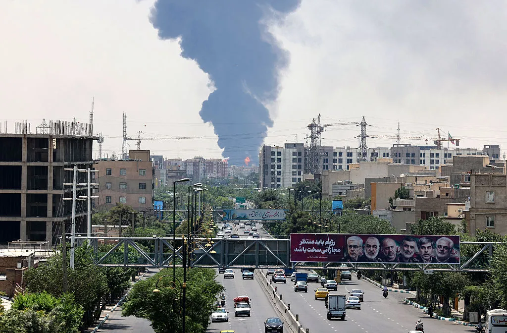 Portraits of Iranian military generals and nuclear scientists,&nbsp;as a plume of heavy smoke rises from an oil refinery in southern Tehran.