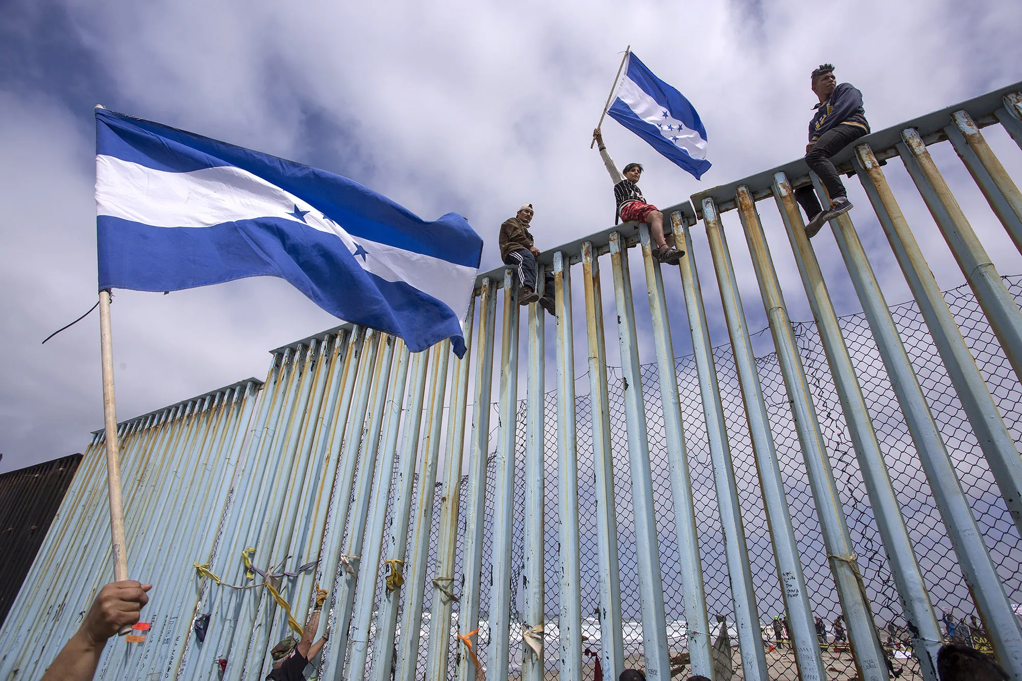 People hold Honduran flags at the border fence during a rally&nbsp;in Tijuana.
