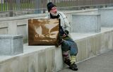 A homeless man sits beside a Gucci shopp