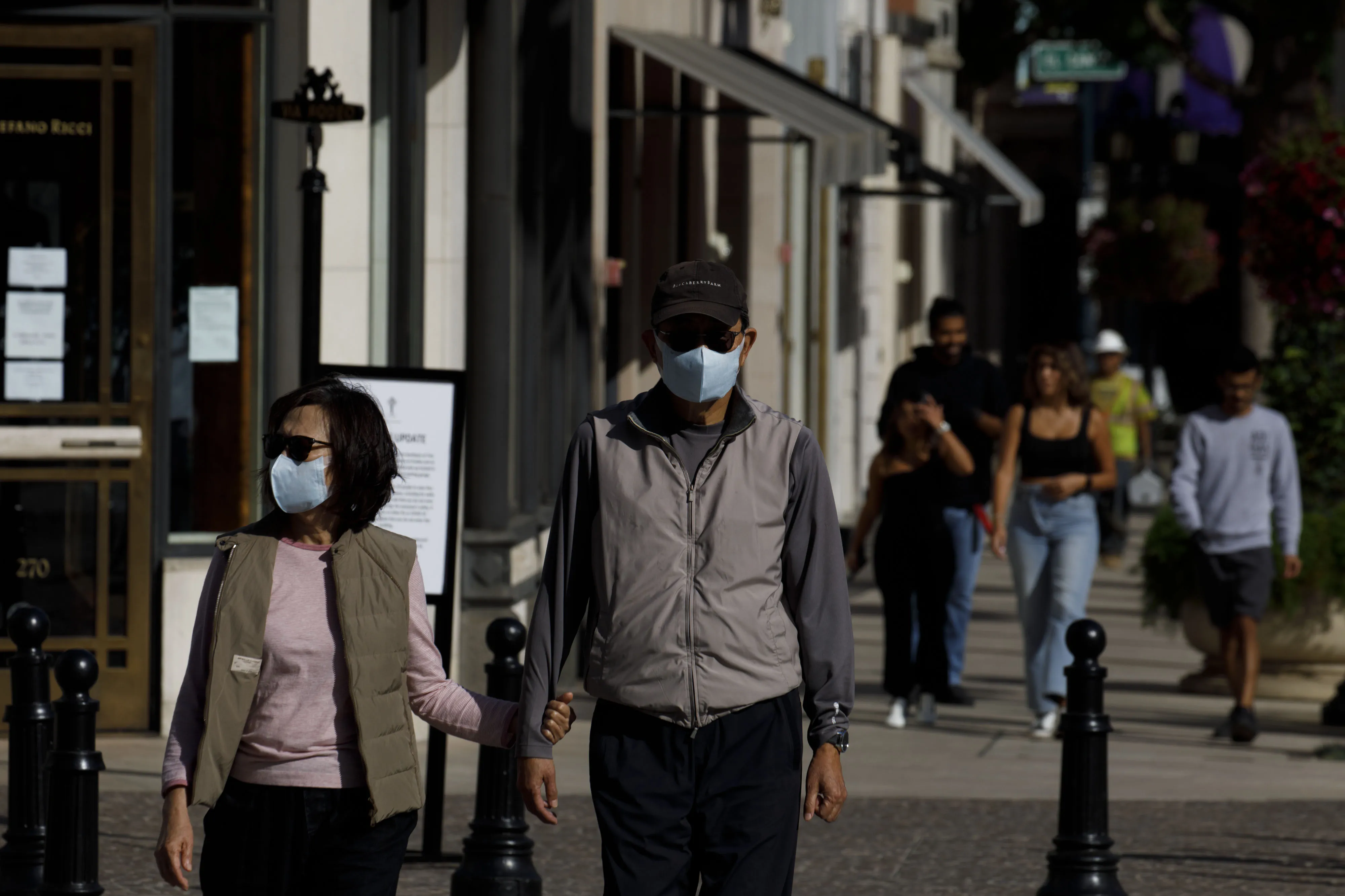 People wear protective masks while walking in front of luxury retail stores on Rodeo Drive in Beverly Hills, California.