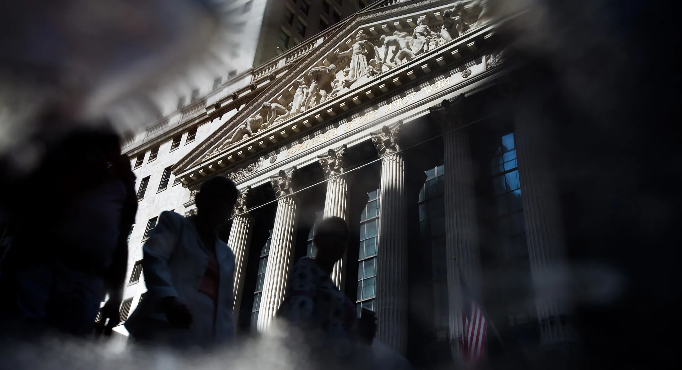 Pedestrians are reflected in a puddle while passing in front of the New York Stock Exchange.
