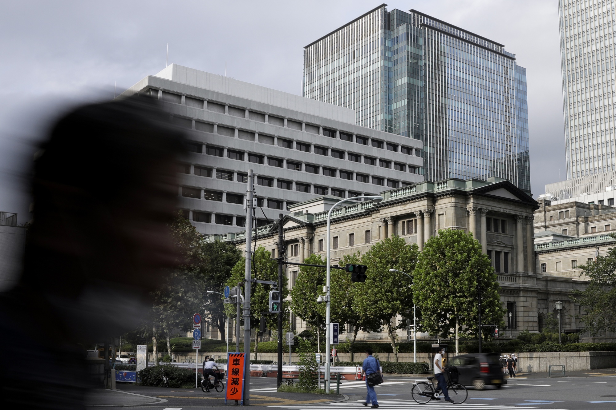 Pedestrians cross a street in front of the Bank of Japan (BOJ) headquarters in Tokyo, Japan, on Monday, September 14, 2020. The Bank of Japan left the bond purchase amount unchanged in a regular operation on Monday.