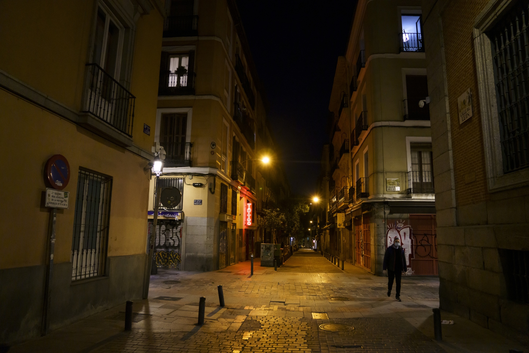 A pedestrian wearing a protective face masks walks by closed cafes and tapas bars at night in Madrid.