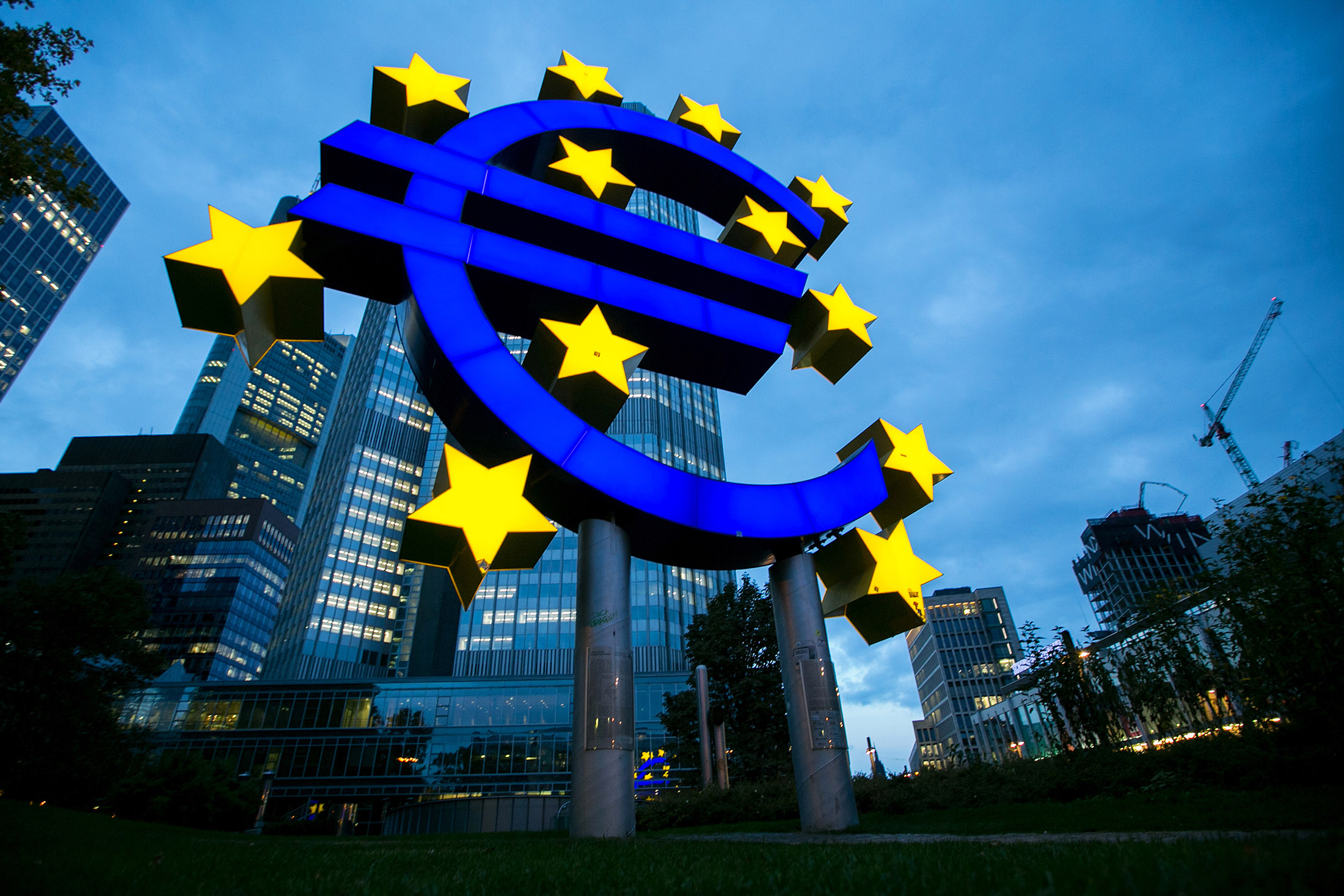 The euro sign sculpture stands illuminated outside the former European Central Bank (ECB) headquarters at dusk in Frankfurt, Germany, on Thursday, Oct. 20, 2016. Unlike Deutsche Bank, which announced plans in June to reduce its branches to 535 from 723 next year, Commerzbank says its branch network is key to its strategy to add two million new clients by 2020, double its previous target.
