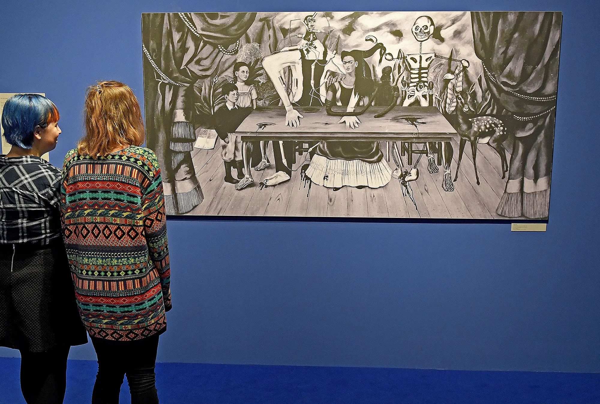 Visitors look at a black-and-white reproduction of "The Wounded Table" by Frida Kahlo.