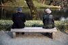 An elderly man and woman sit on opposite ends of a park bench