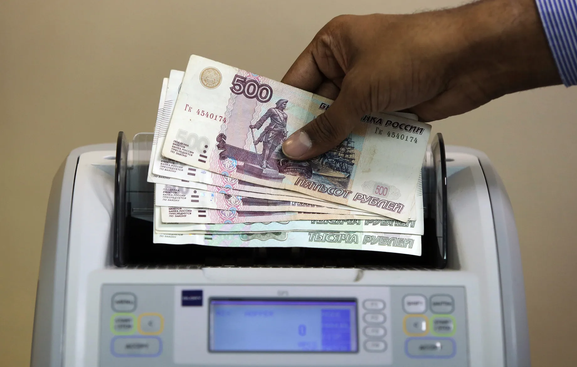 An employee loads Russian ruble banknotes into a counting machine.&nbsp;