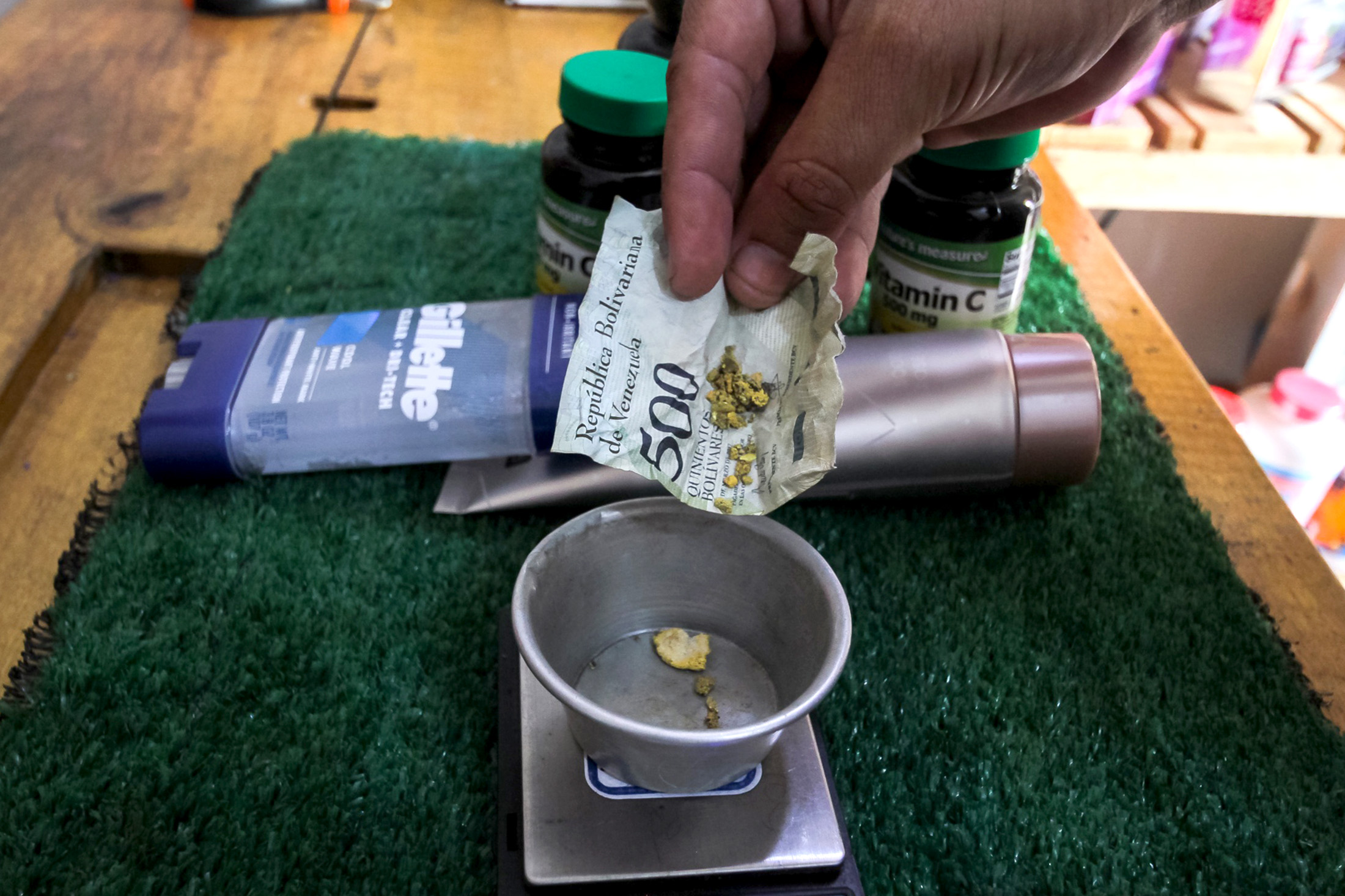 A customer places gold wrapped in a crumpled bolivar banknote on to a scale for payment at a pharmacy in Tumeremo, Venezuela.