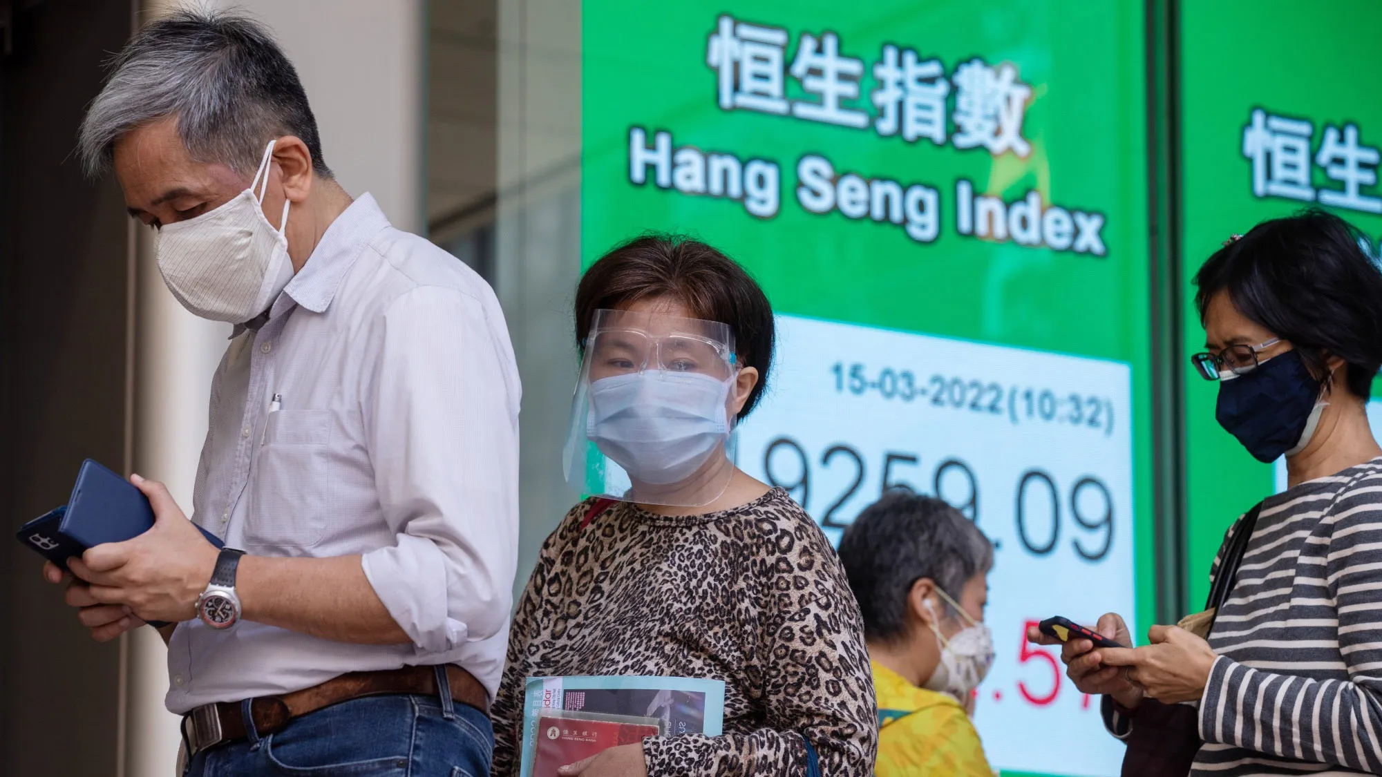 Pedestrians pass an electronic screen displaying the Hang Seng Index in Hong Kong, on March 15.