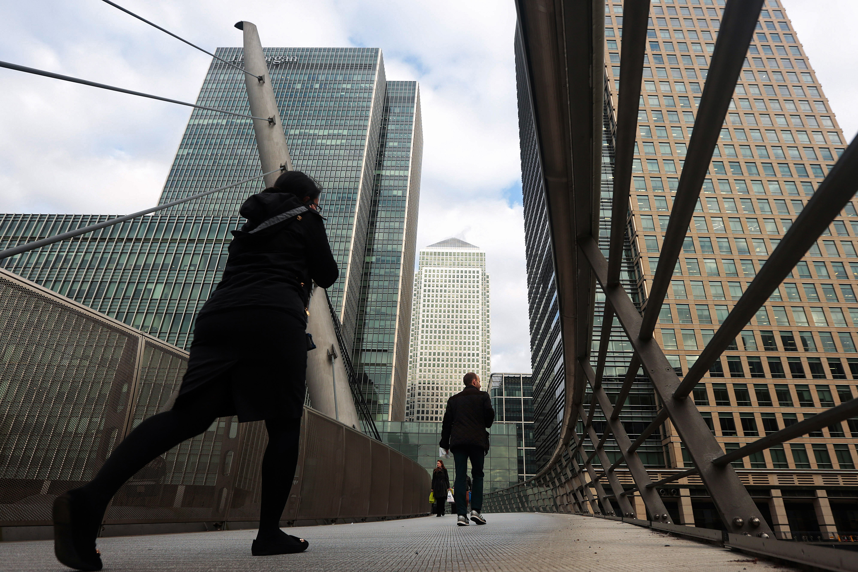 Pedestrians cross a bridge near the offices of JPMorgan Chase &amp; Co., left, and the One Canada Square office building, center, in the Canary Wharf business, financial and shopping district of London. Photographer: Jason Alden/Bloomberg
