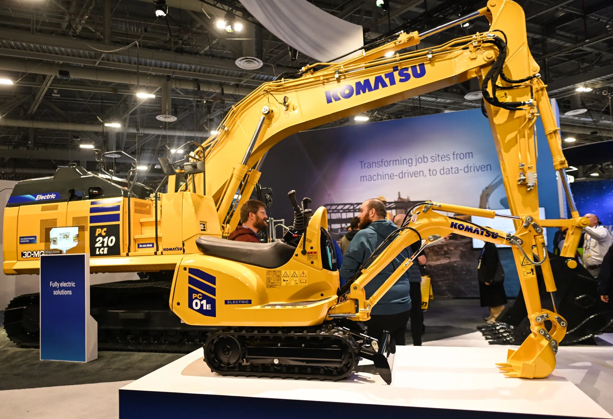 Komatsu’s PC01E-2 micro-excavator sits alongside its 20-ton sibling, the PC210LCE-11, during CES 2025 in Las Vegas in 2025. Both are fully electric.