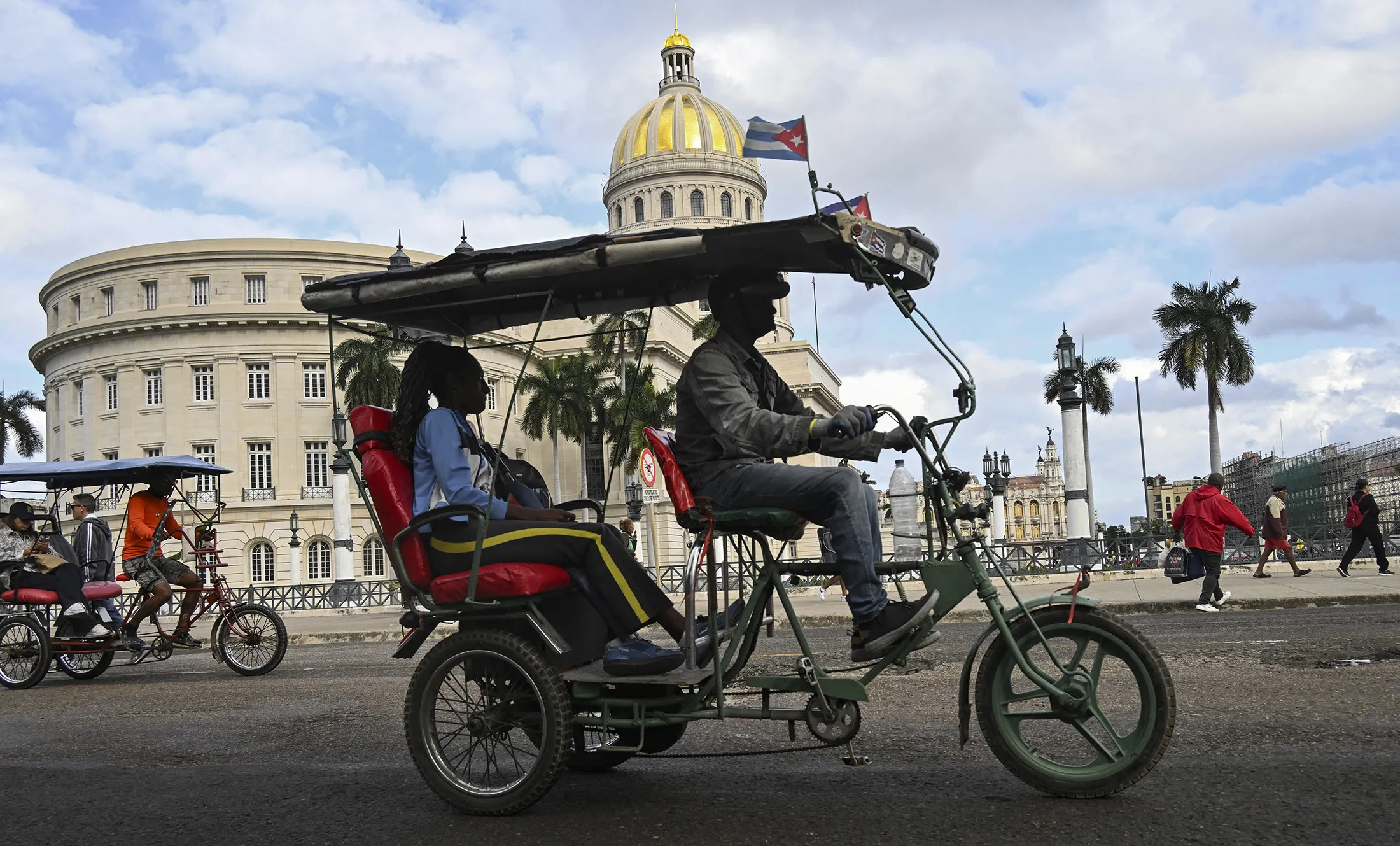 A tricycle taxi decorated with the Cuban flag passes near the Capitolio in Havana on Jan. 30.