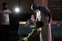 A health worker takes swab samples under the light of a colleague’s mobile phone at the Jawahar Lal Nehru Stadium in New Delhi, on April 16.