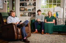 Ryan Turman sits on a chair, looking at his cell phone, as his son Hudson and wife Lacey sit nearby on a sofa in Amarillo, Texas