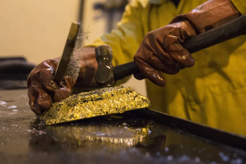 A mine worker hammers a large ingot of gold.