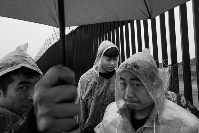 Chinese asylum seekers wait  in the rain at a section of the US-Mexico border wall for CBP agents to register and process them. 