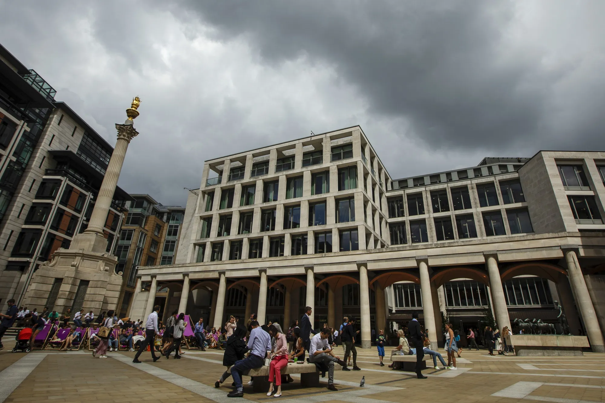 Pedestrians sit outside the London Stock Exchange.