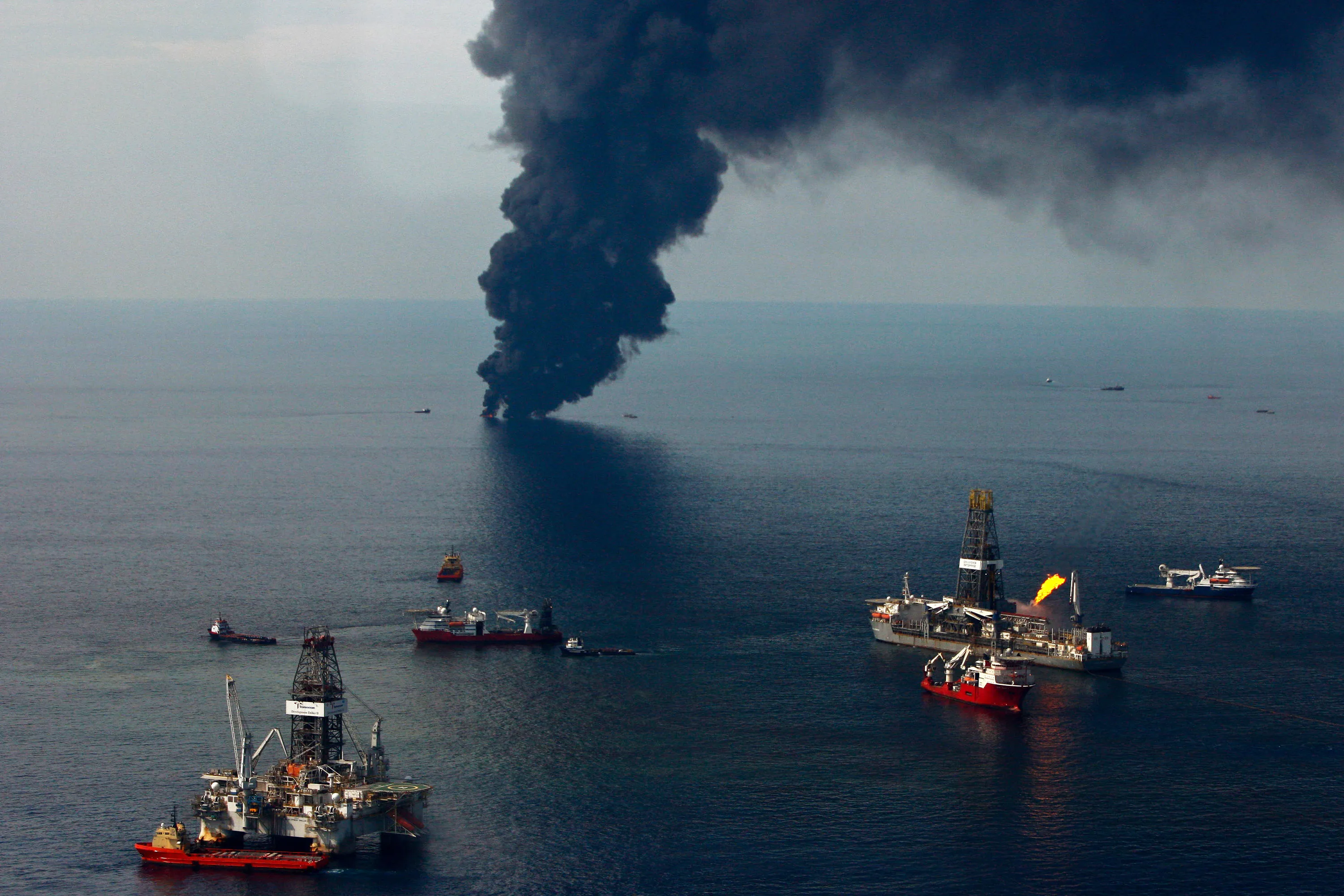 Smoke rises from controlled oil burns of oil on the surface of the water as the Development Driller II, left, and Discoverer Enterprise work at the site of the Deepwater Horizon oil spill in the Gulf of Mexico off the coast of Louisiana, on&nbsp;June 19, 2010.