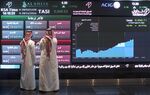 Visitors stand and watch stock movements displayed on large video screens inside the Saudi Stock Exchange.