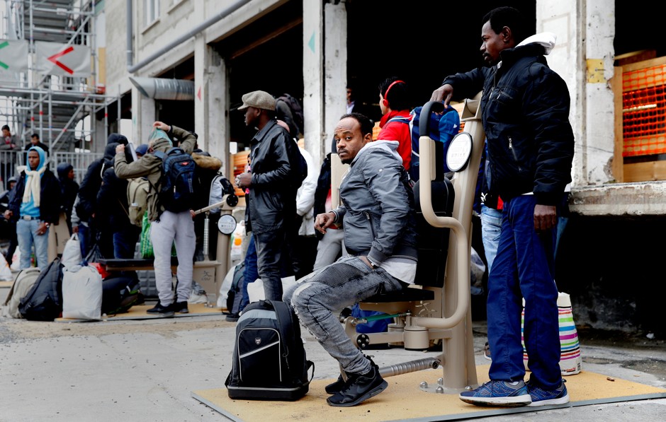 People wait for a bus to leave the reception center for migrants and refugees near Porte de La Chapelle.