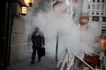 A pedestrian passes in front of a tube releasing a cloud of steam near the New York Stock Exchange (NYSE).