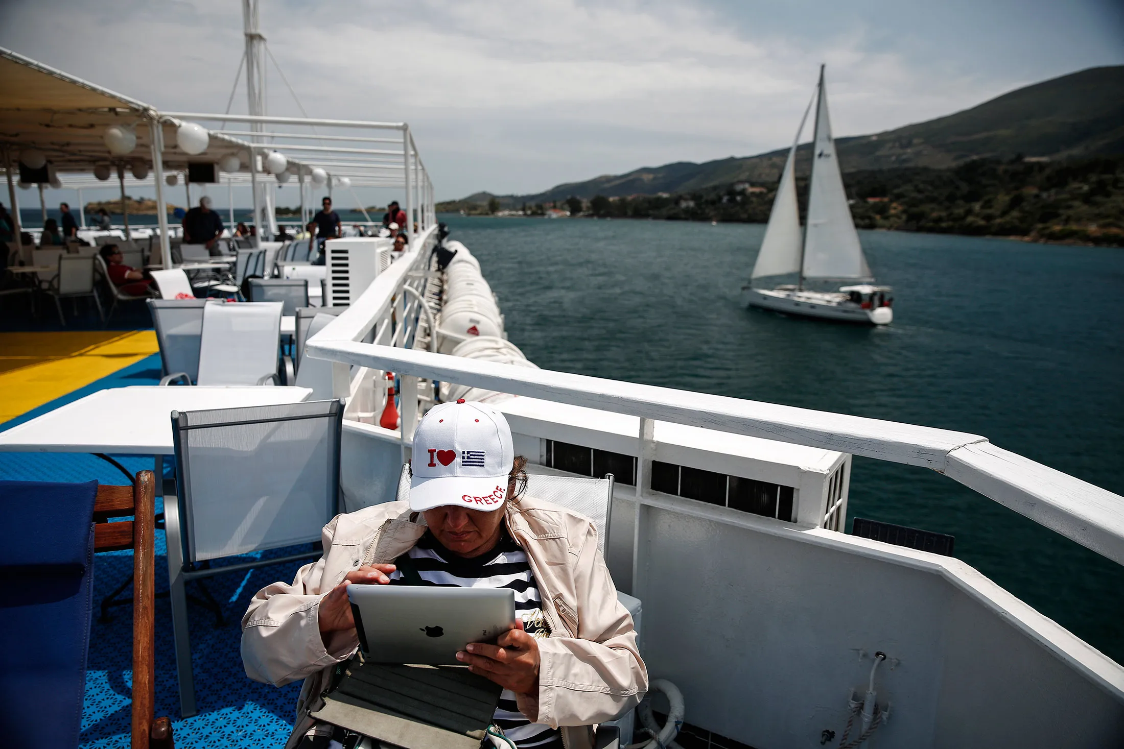 A tourist wearing an "I Love Greece" cap checks her Apple Inc. iPad as she sails aboard a cruise ship in the Saronic gulf, west of Athens, Greece, on May 11, 2015.
