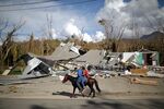 Local residents ride a horse by a house wiped out by Hurricane Maria in Jayuya, Puerto Rico.