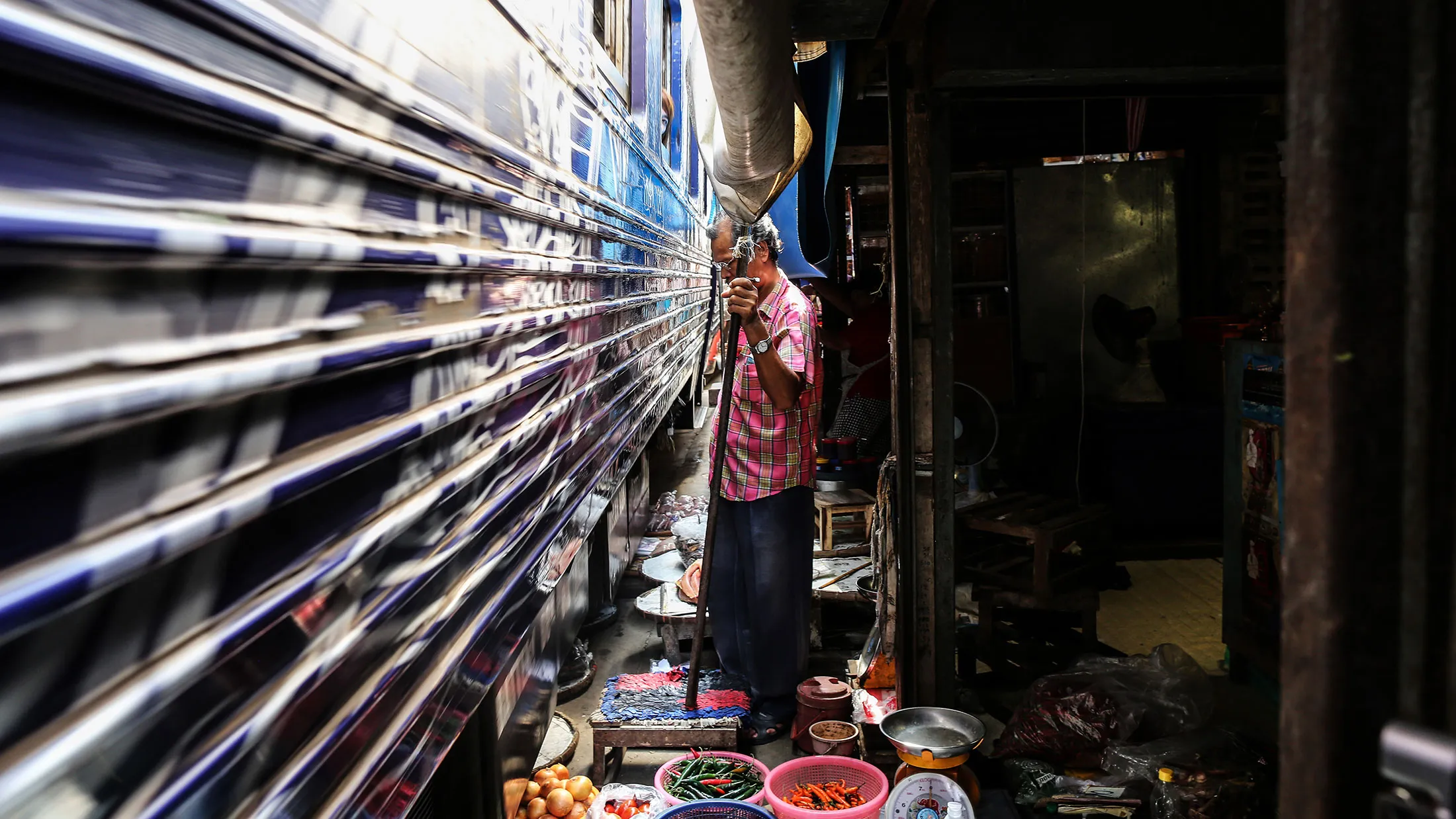 A vendor holds a pole that supports the awnings of his market stall as a train travels through the Maeklong Railway Market in Samut Songkram, Thailand.
