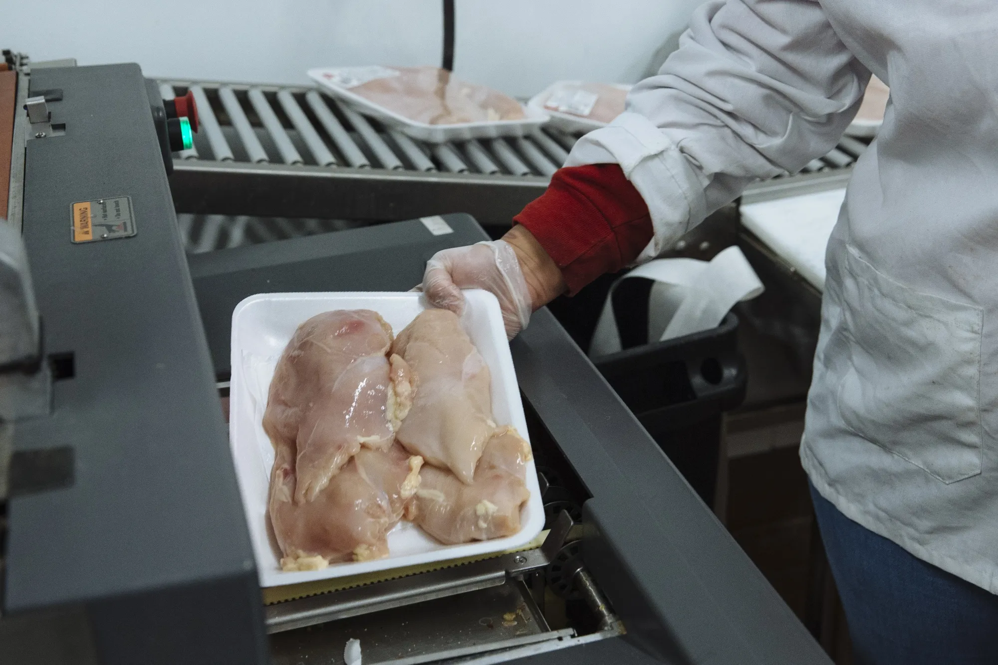 A worker places chicken breasts in a machine to be weighed and packaged in the butcher section of a supermarket.