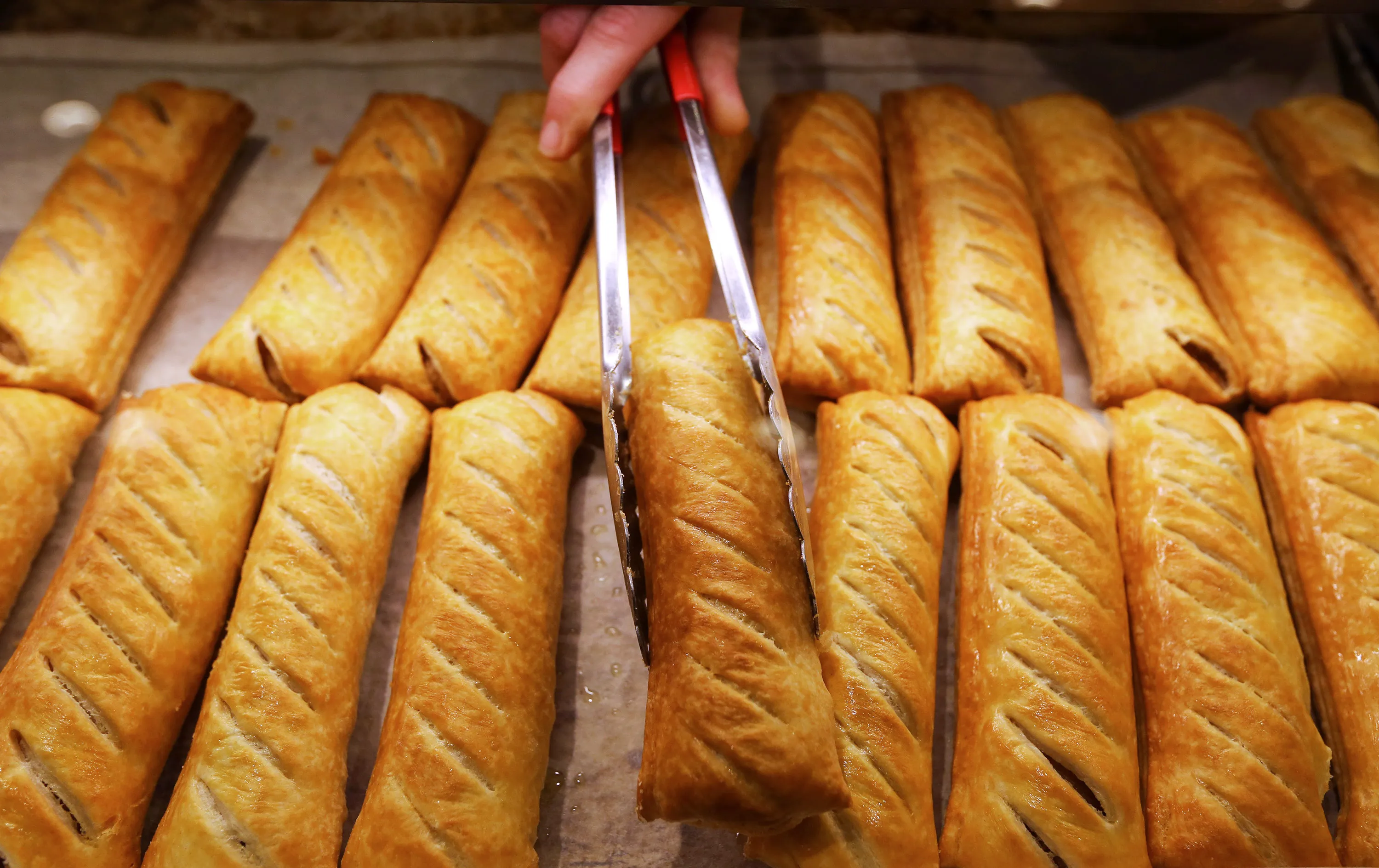 An employee uses tongs to remove a sausage roll from the counter in a Greggs Plc sandwich chain outlet in Caterham, U.K., on Thursday, Oct. 22, 2015. Same-store sales at Greggs have grown 5.6 percent so far in 2015, up from 3.9 percent across the same period last year, and the company said on Oct. 6 that full-year growth will exceed its previous forecast slightly.