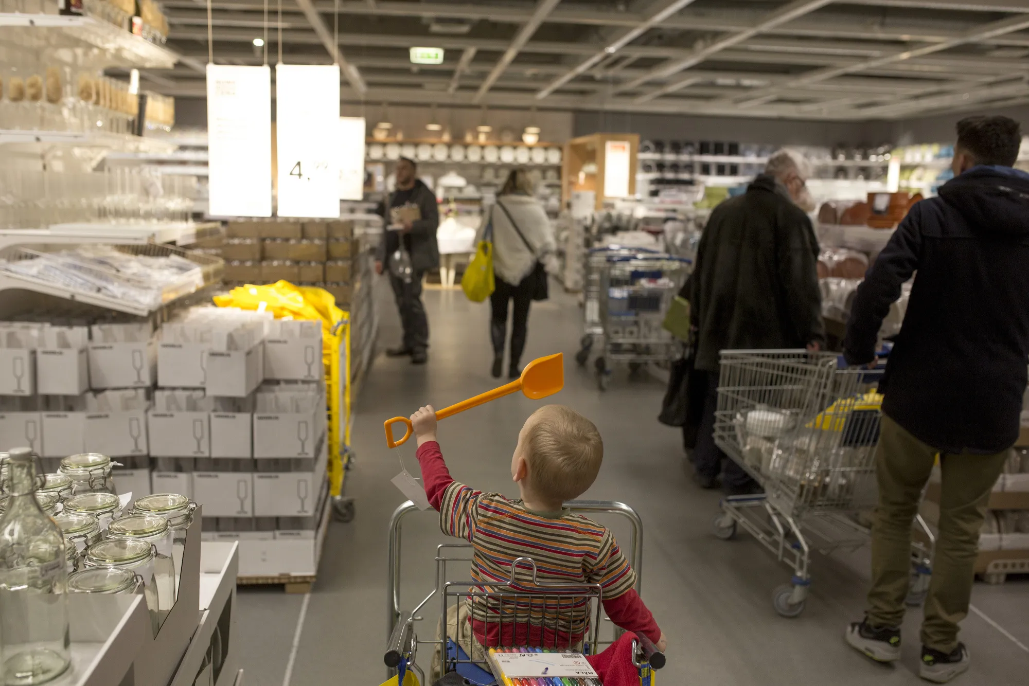 A child plays with a plastic spade while sitting in a shopping cart as customers browse goods inside an Ikea AB store in Poznan, Poland.
