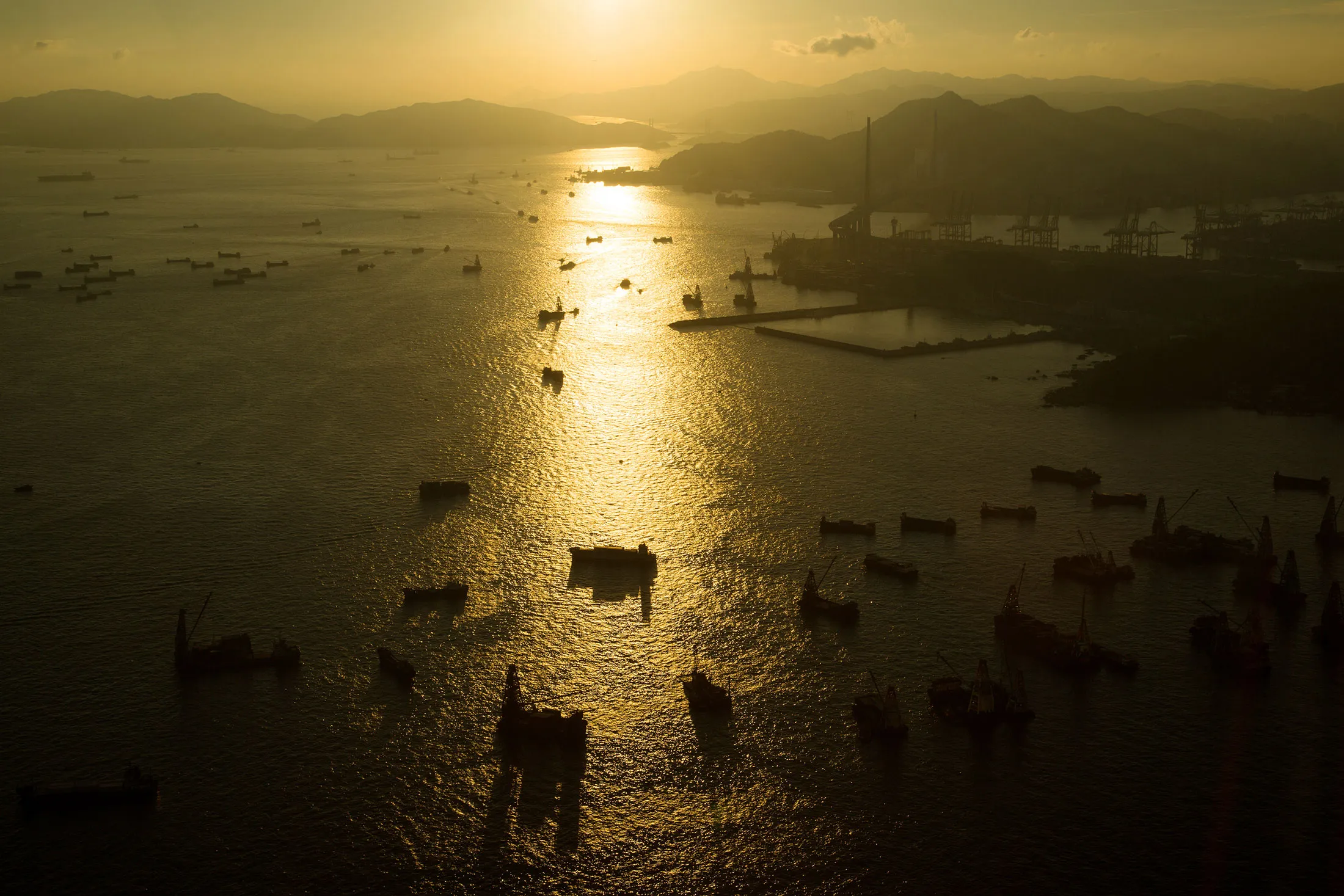 Ships sail through Victoria Harbor at sunset near the the Kwai Tsing Container Terminals, right, in Hong Kong, China.
