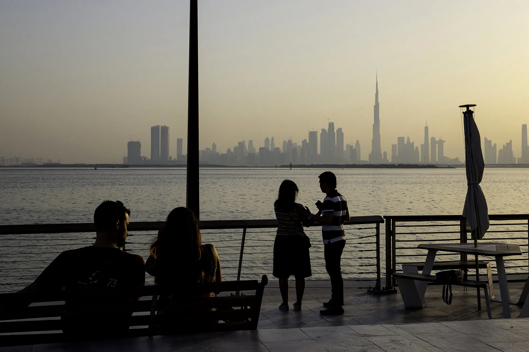 People watch the sun set from the Dubai Creek Habour Development looking out towards the Burj Khalifa tower, center, and other skyscrapers in Dubai, United Arab Emirates.