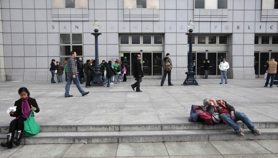 A homeless man sits on the steps of the San Francisco Public Library.