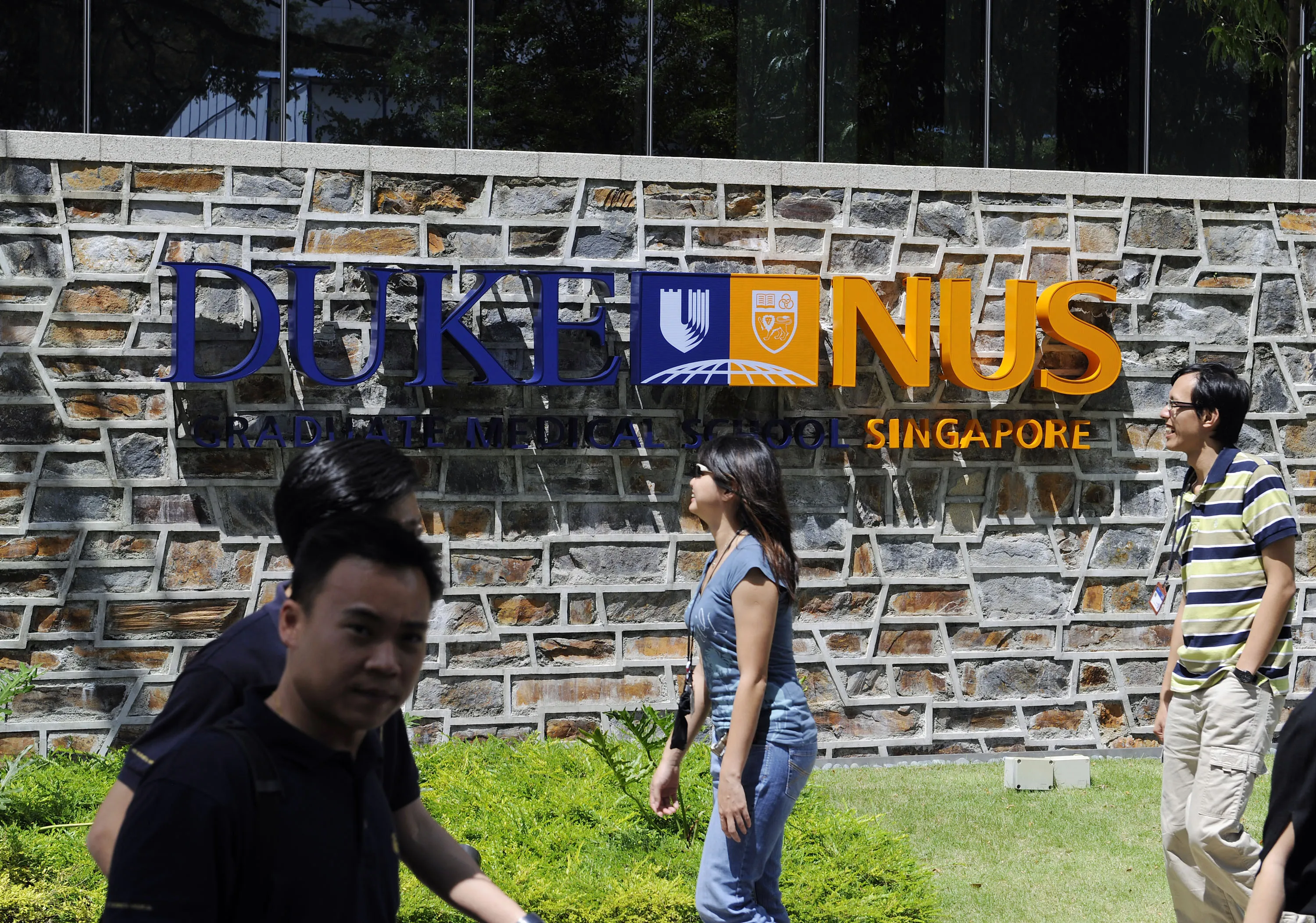 People walk past a sign for the Duke-NUS (National University of Singapore) Graduate Medical School in Singapore. Photographer: Munshi Ahmed/Bloomberg
